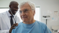   Healthcare provider in a lab coat standing behind a patient in a blue hospital gown checking their vitals