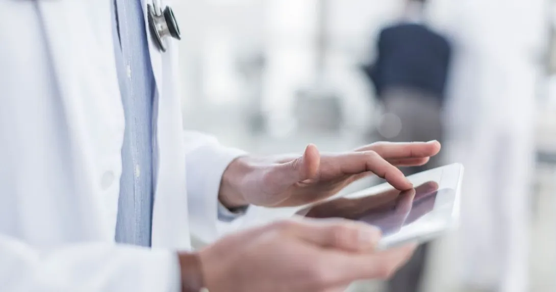 Healthcare provider wearing a lab coat with a stethoscope around their neck while holding a tablet