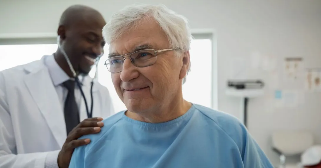 Healthcare provider in a lab coat standing behind a patient in a blue hospital gown checking their vitals Healthcare provider in a lab coat standing behind a patient in a blue hospital gown checking their vitals