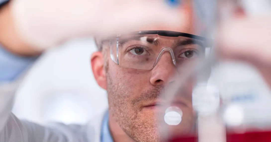 Scientist in a laboratory filling up a beaker while wearing safety goggles Scientist in a laboratory filling up a beaker while wearing safety goggles